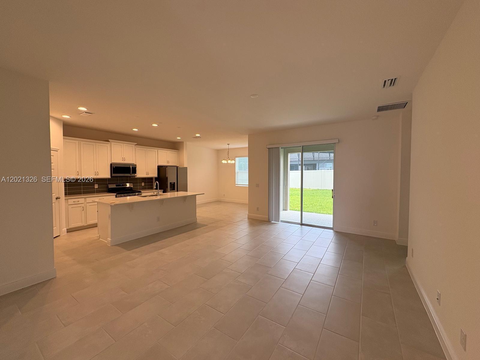 An open-concept kitchen with white cabinets and an island overlooks a living area with tile floors — 366 SWITCHGRASS LOOP # 366, Other City - In The State Of Florida FL 34715, OTHER CITY - IN THE STATE OF FLORIDA, FL