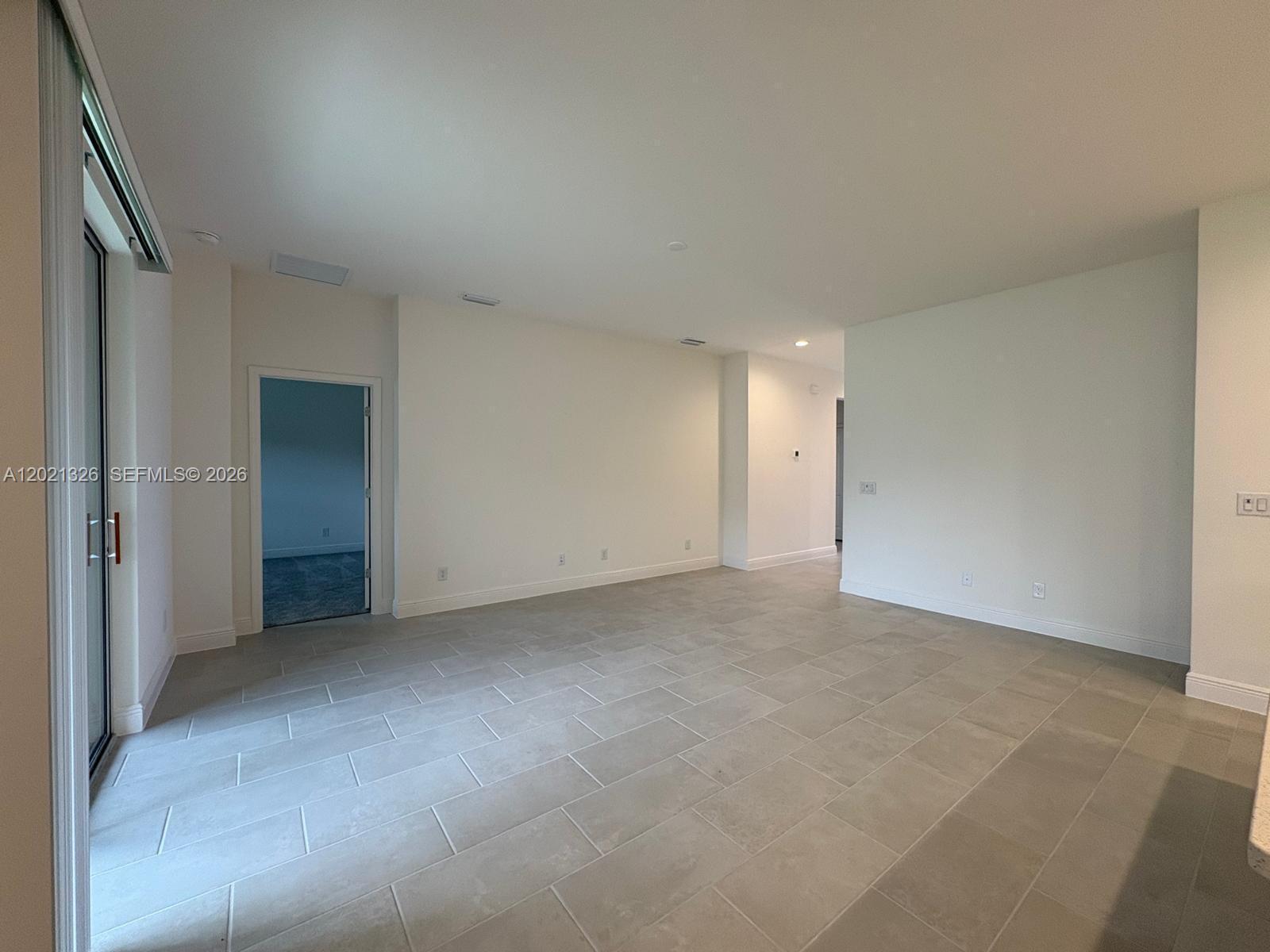 An empty room features light gray tile flooring, white walls, and a sliding glass door — 366 SWITCHGRASS LOOP # 366, Other City - In The State Of Florida FL 34715, OTHER CITY - IN THE STATE OF FLORIDA, FL