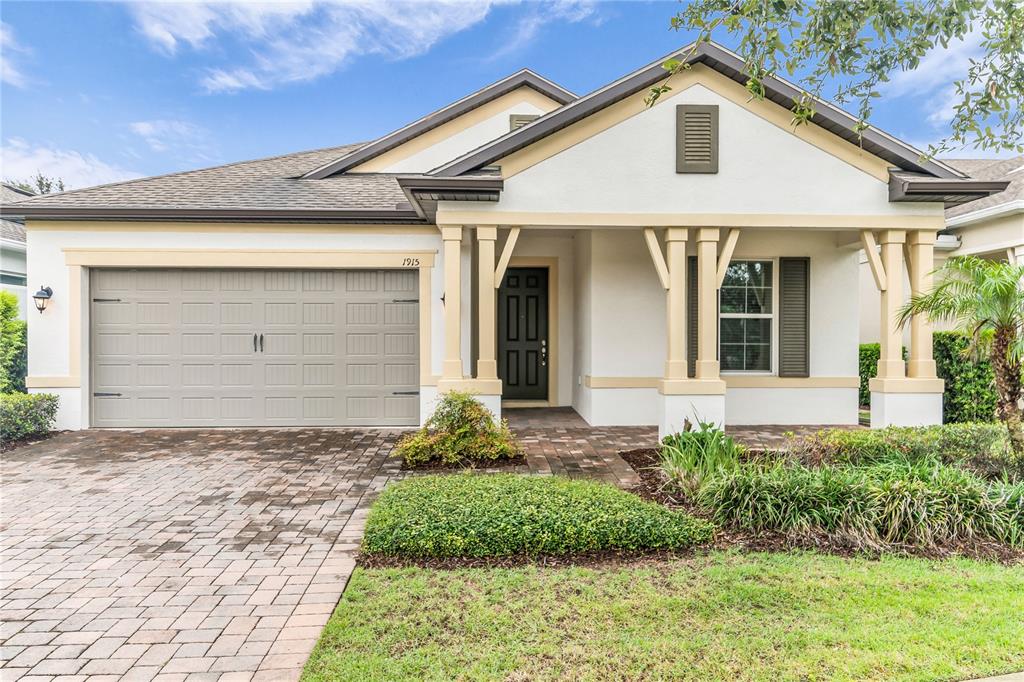 A single-story house with a beige garage, white stucco walls, and a covered front porch — 1915 ESTUARY LANE, KISSIMMEE, FL