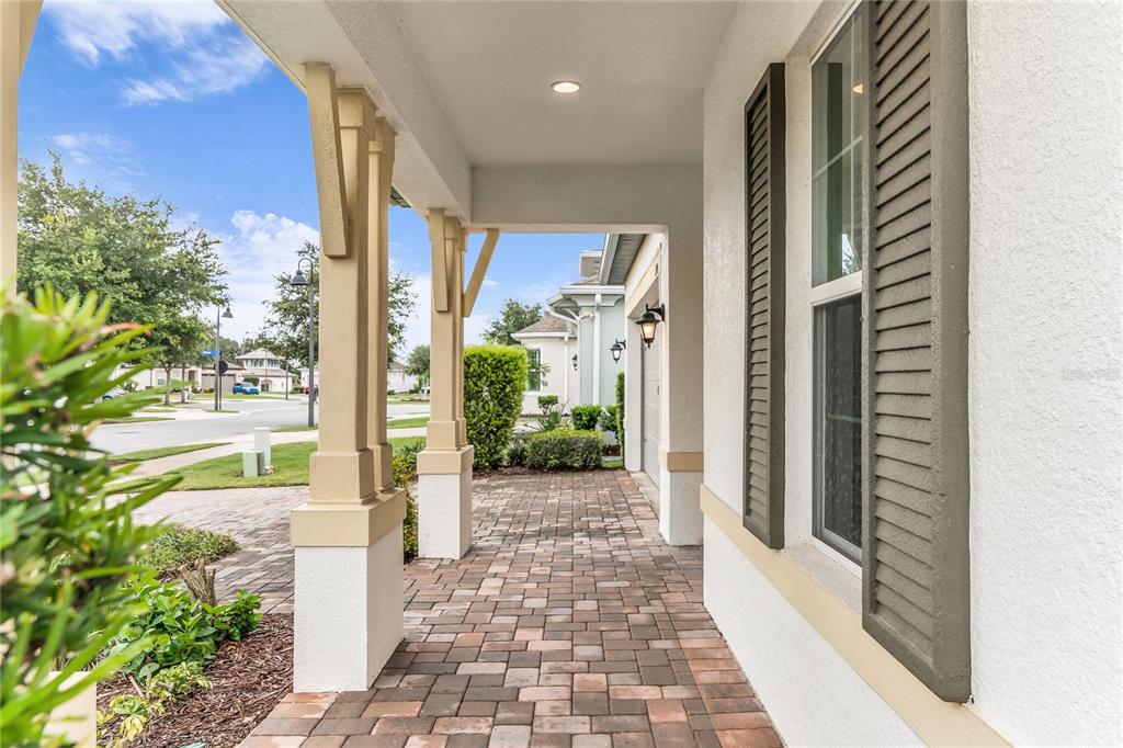A covered entryway features a dark front door, a window with shutters, and paver flooring — 1915 ESTUARY LANE, KISSIMMEE, FL