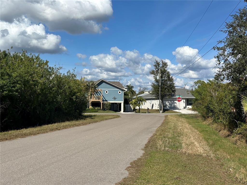 A paved road leads toward two houses under a blue sky with scattered clouds — 1460 WESTOVER STREET, PORT CHARLOTTE, FL