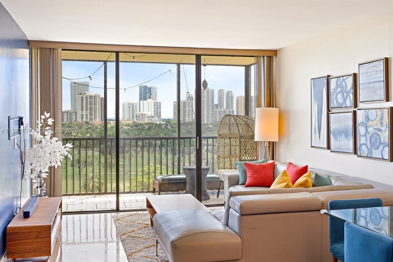 A living room features a beige sectional sofa, a balcony with a city view, and tiled floors — 20335 W Country Club Dr # 1208, Aventura FL 33180, AVENTURA, FL