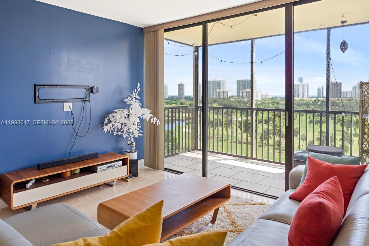 A living room with a blue accent wall, media console, and balcony overlooking a golf course — 20335 W Country Club Dr # 1208, Aventura FL 33180, AVENTURA, FL
