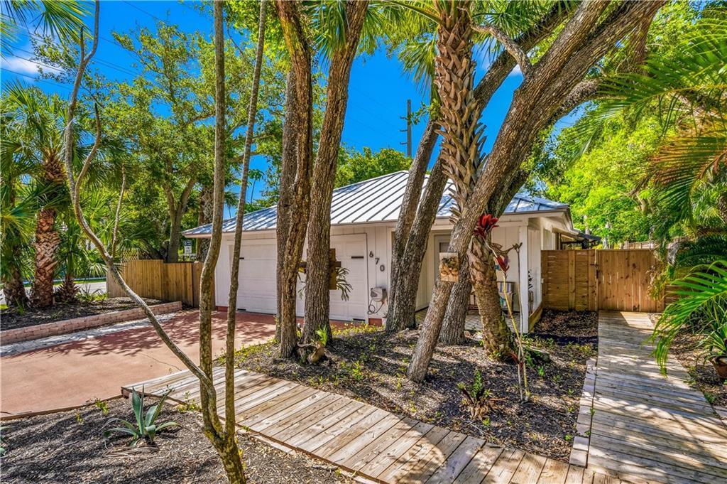 A small white house with a metal roof surrounded by palm trees and wooden walkways — VERO BEACH, FL
