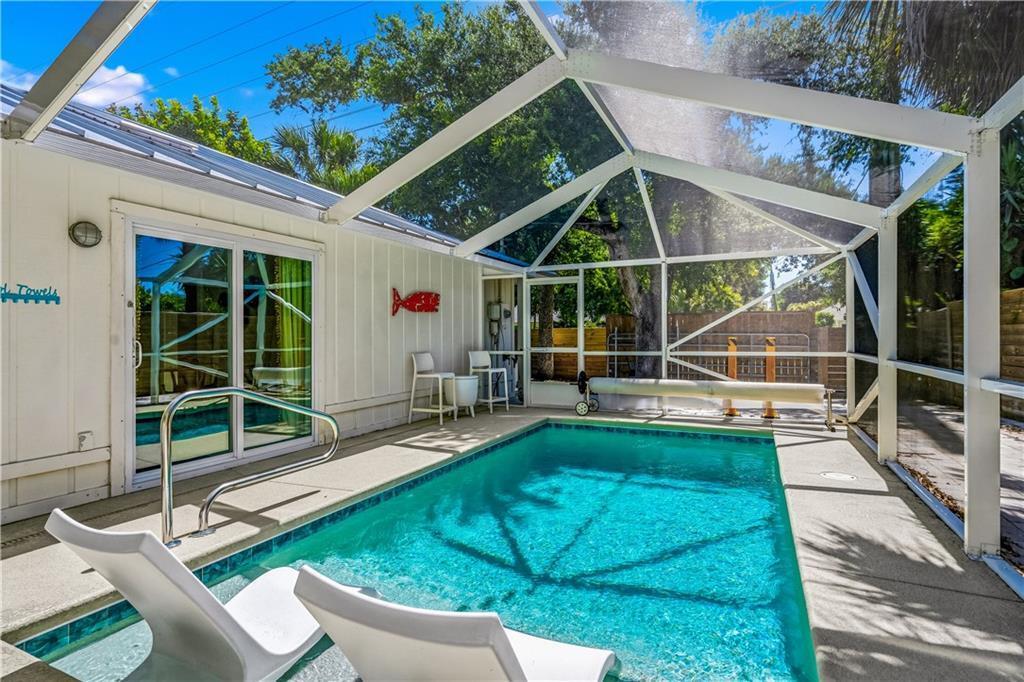 A screened-in patio features a rectangular swimming pool with two lounge chairs and a sliding door — VERO BEACH, FL