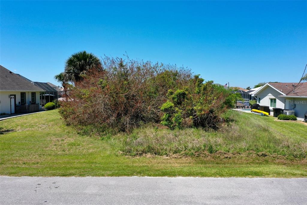 A vacant, overgrown residential lot sits between two existing houses under a clear blue sky — 17 CLARIDGE COURT N, PALM COAST, FL