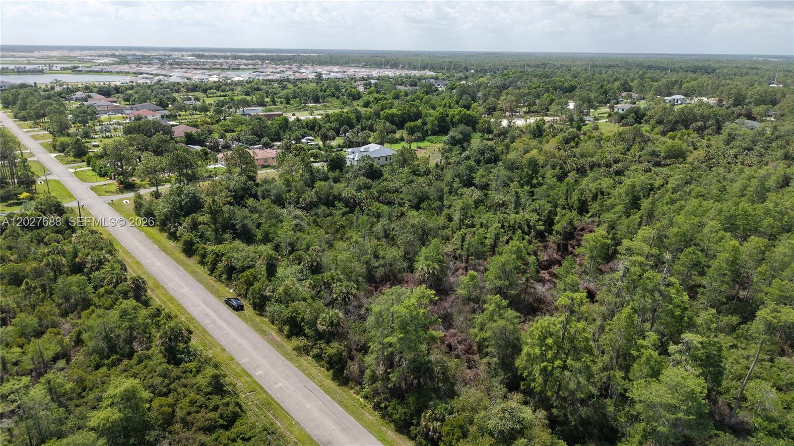 An aerial view shows a paved road running alongside a large, densely wooded vacant lot — 0 37th Avenue NE, Naples FL 34120, NAPLES, FL