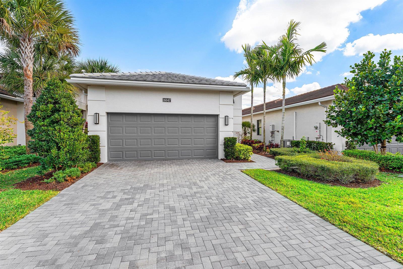 A single-story house exterior features a gray garage door, paved driveway, and tropical landscaping — 16047 Key Biscayne Lane, Westlake FL 33470, WESTLAKE, FL