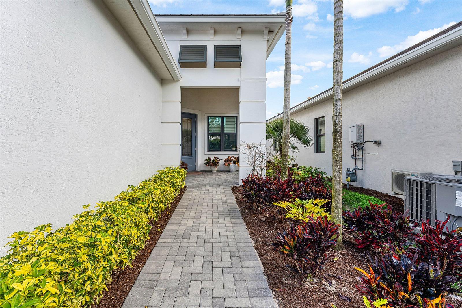 A paved walkway leads to the front entrance of a white house with landscaped gardens — 16047 Key Biscayne Lane, Westlake FL 33470, WESTLAKE, FL
