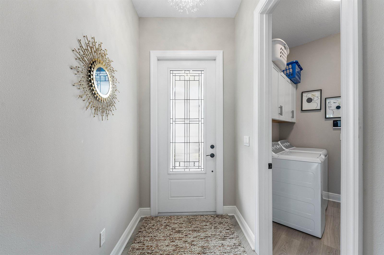 An entryway with a decorative mirror and front door leads into a laundry room — 16047 Key Biscayne Lane, Westlake FL 33470, WESTLAKE, FL