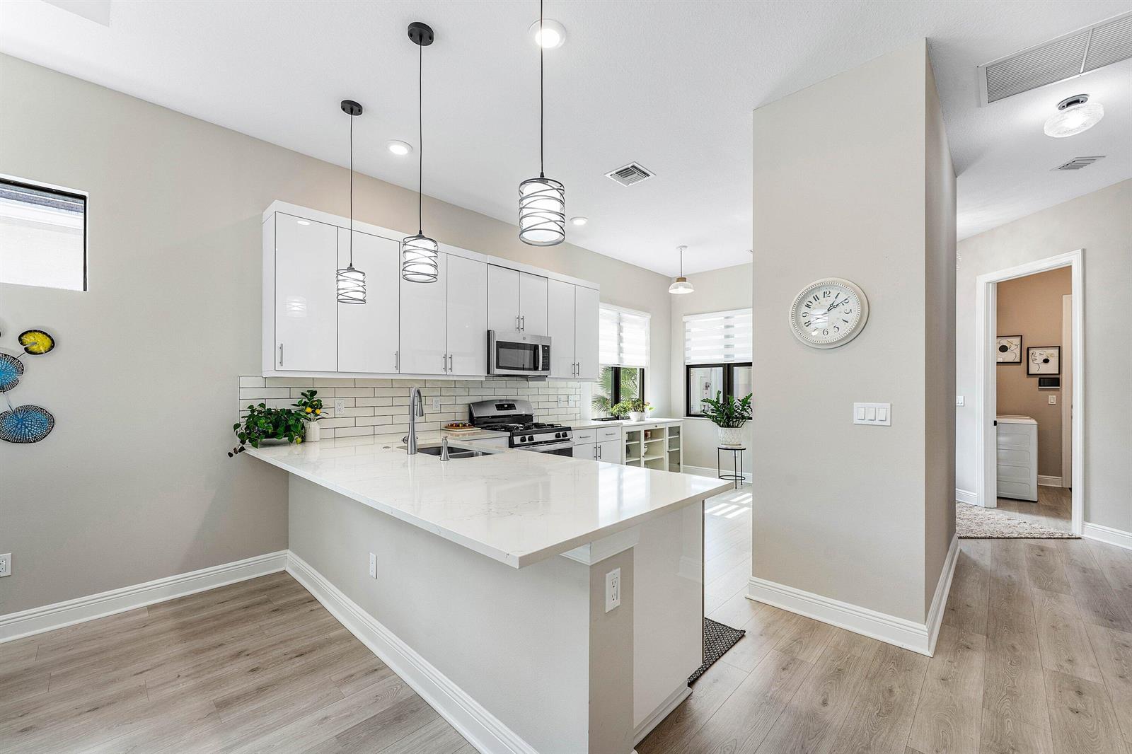 A modern kitchen features white cabinets, quartz countertops, a breakfast bar, and light wood flooring — 16047 Key Biscayne Lane, Westlake FL 33470, WESTLAKE, FL