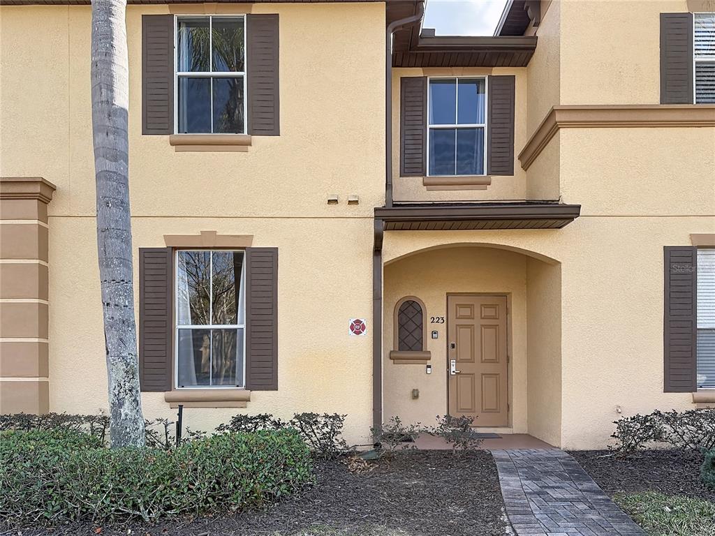 The exterior of a two-story tan stucco townhouse features brown shutters and a front door — 223 NAPOLI DRIVE, DAVENPORT, FL
