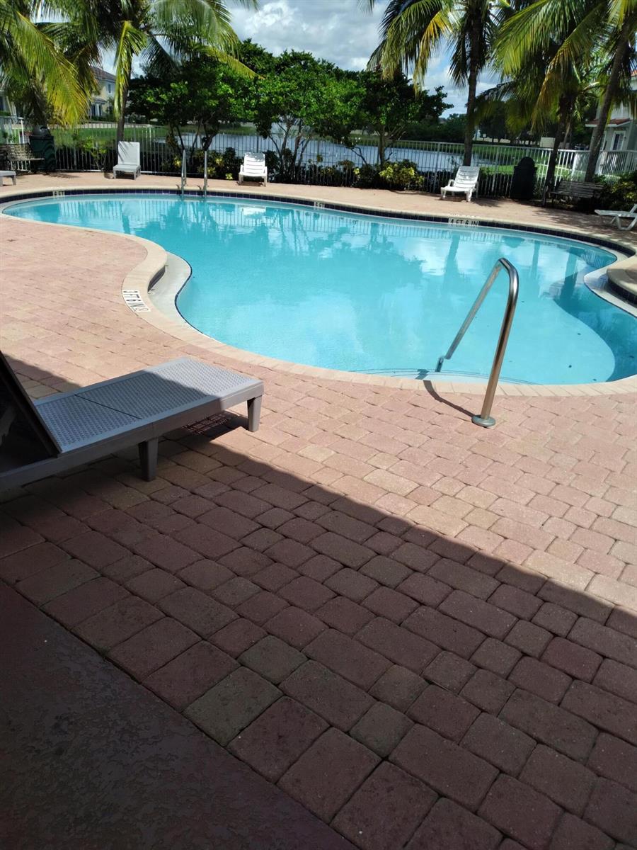 A swimming pool with a brick paver deck and lounge chairs sits beside a lake — 2615 SW 81st Terrace # 2599, Miramar FL 33025, MIRAMAR, FL