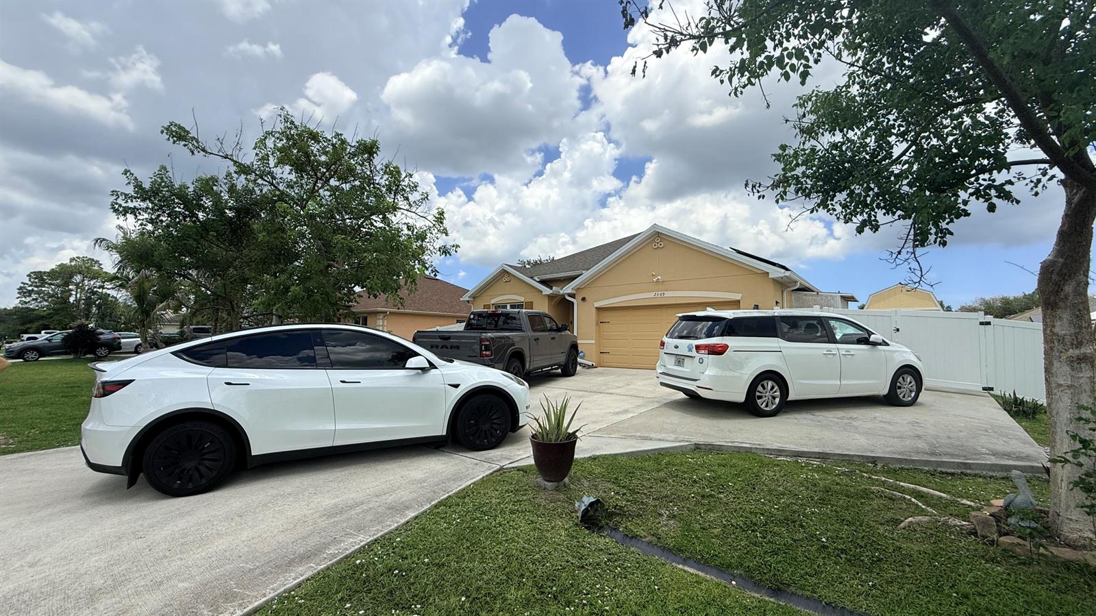 A single-story house with a tan exterior, a two-car garage, and three vehicles parked outside — 2369 SW Barber Lane, Port St. Lucie FL 34984, PORT ST. LUCIE, FL