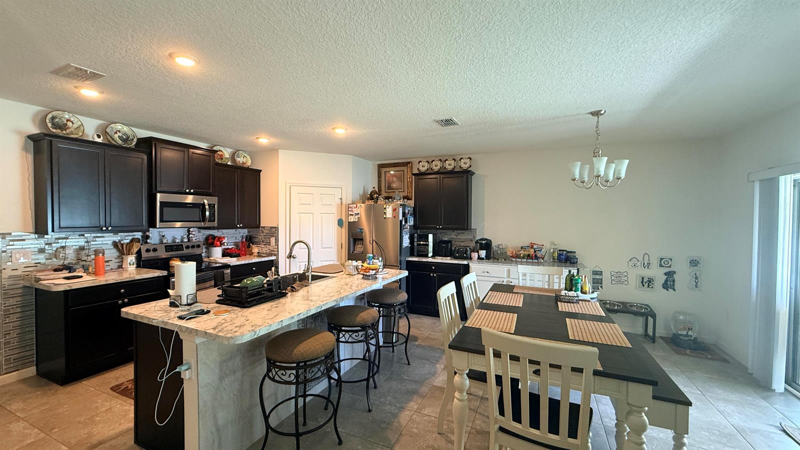 A kitchen features dark cabinetry, a marble-topped island with bar seating, and an adjacent dining area — 2369 SW Barber Lane, Port St. Lucie FL 34984, PORT ST. LUCIE, FL