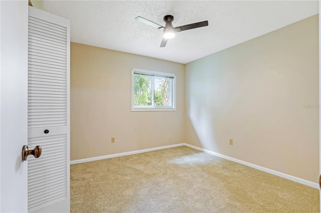 An empty bedroom features beige walls, tan carpeting, a ceiling fan, and a louvered closet door — 19 BANNER LANE, PALM COAST, FL