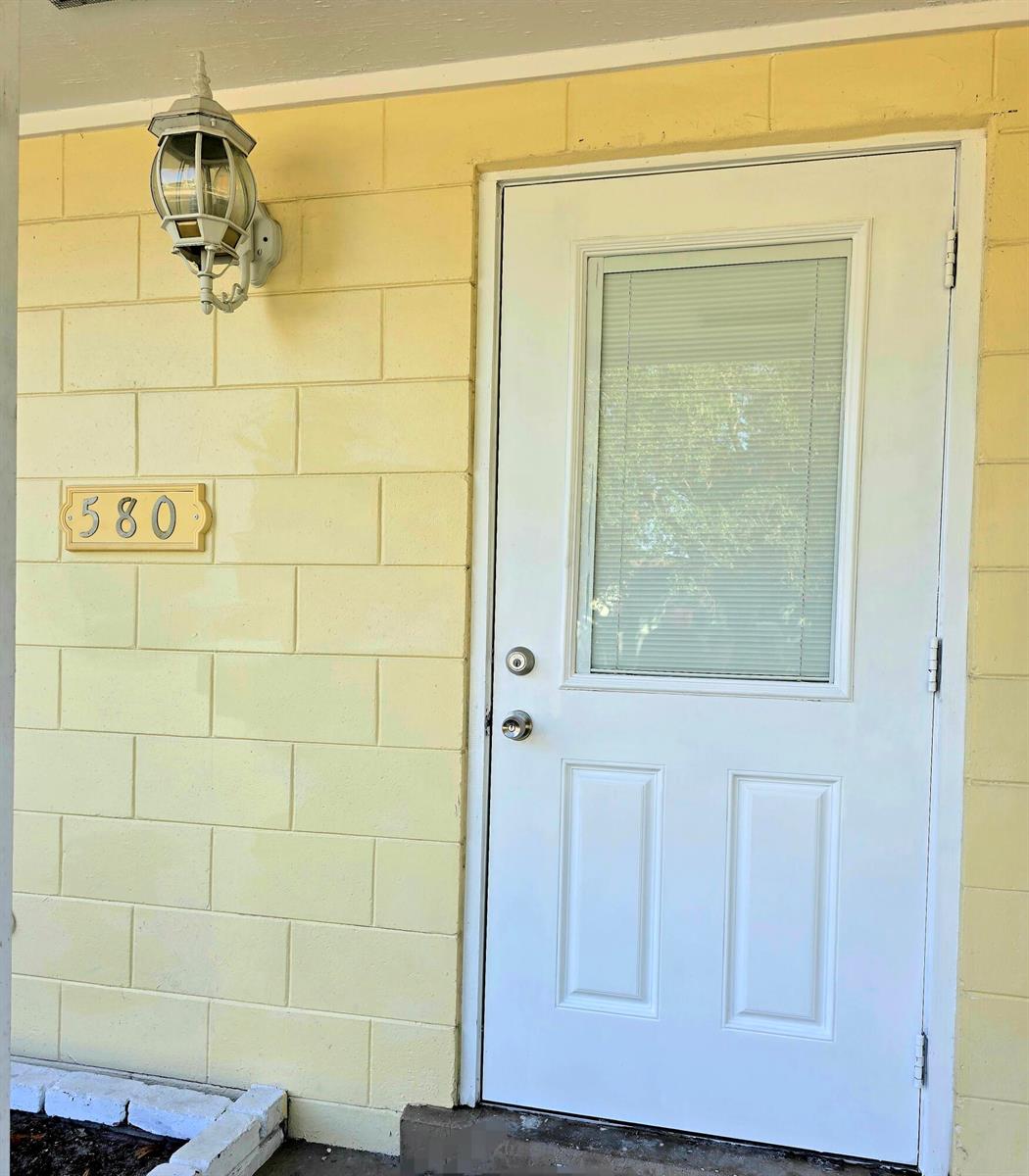A white door with a glass insert sits next to a house number on a yellow wall — 580 Wendell Road, Fort Pierce FL 34950, FORT PIERCE, FL