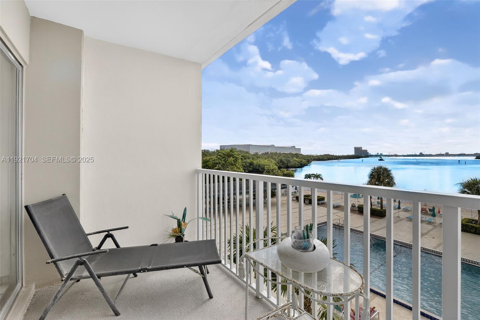 A balcony features a lounge chair, a small glass table, and a view of a pool — 300 Bayview Dr # 308, Sunny Isles Beach FL 33160, SUNNY ISLES BEACH, FL