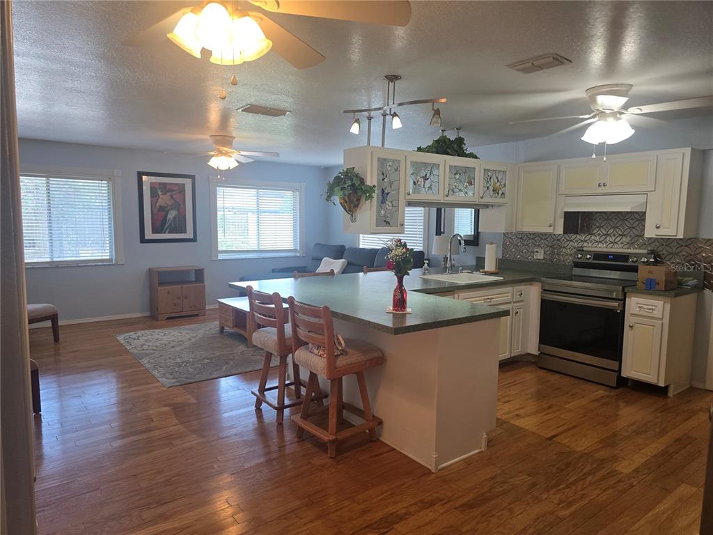 An open-concept kitchen and living area features wood flooring, a breakfast bar, and ceiling fans — 8431 PAMLICO STREET, ORLANDO, FL