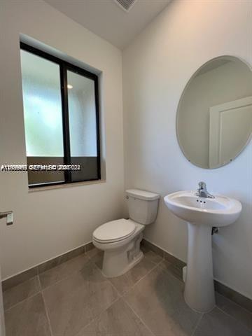 A bathroom features a pedestal sink, a toilet, a round mirror, and a window — 327 NE 208th Ter, Miami FL 33179, MIAMI, FL