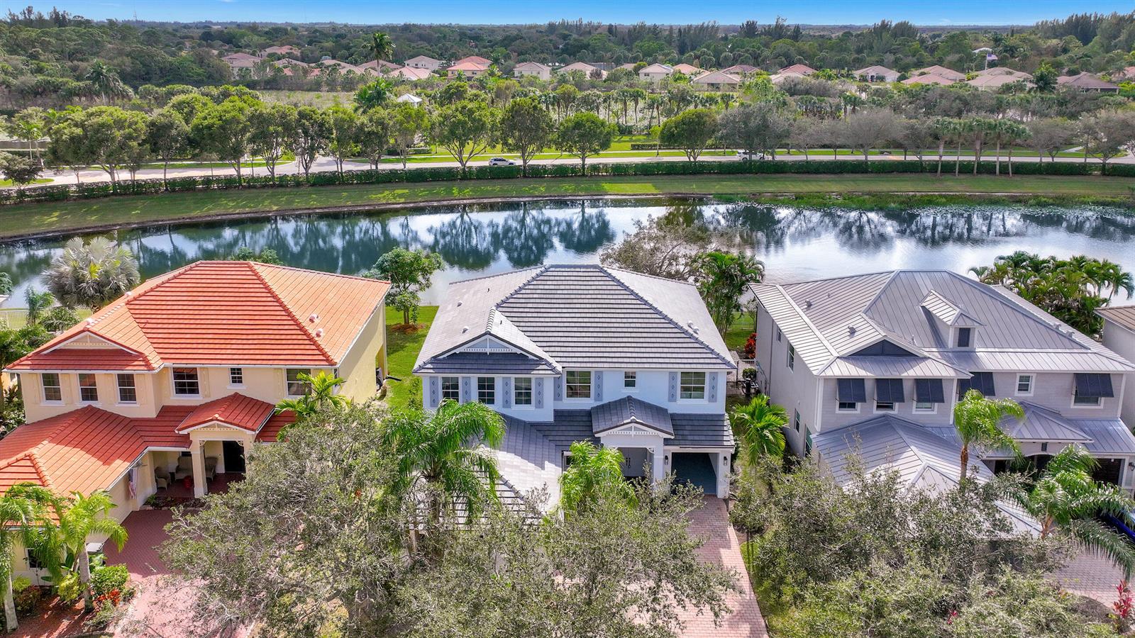 An aerial view shows three suburban houses with tiled roofs situated along a lake — 9334 Madewood Court, Royal Palm Beach FL 33411, ROYAL PALM BEACH, FL