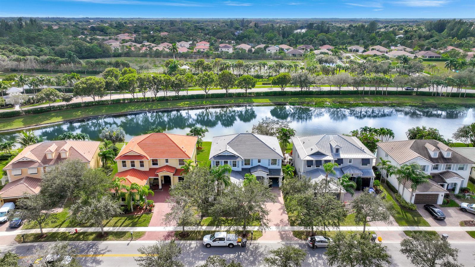 An aerial view shows a row of suburban houses facing a lake and green space — 9334 Madewood Court, Royal Palm Beach FL 33411, ROYAL PALM BEACH, FL