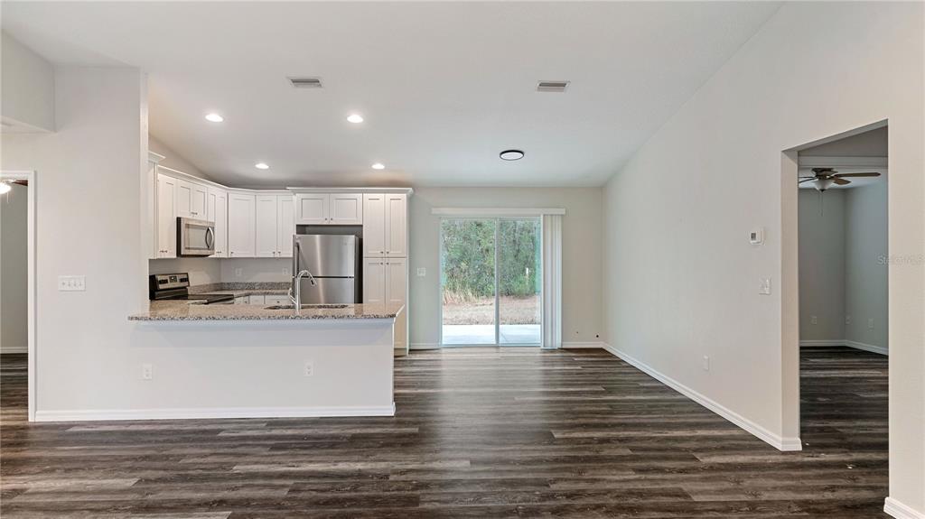 A kitchen with white cabinets and granite countertops opens to a living area with flooring — 296 OAK LANE TRACK, OCALA, FL