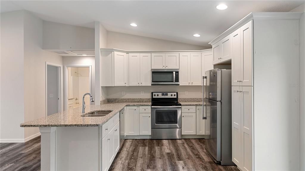 A kitchen features white cabinetry, stainless steel appliances, and a granite-topped island with a sink — 296 OAK LANE TRACK, OCALA, FL