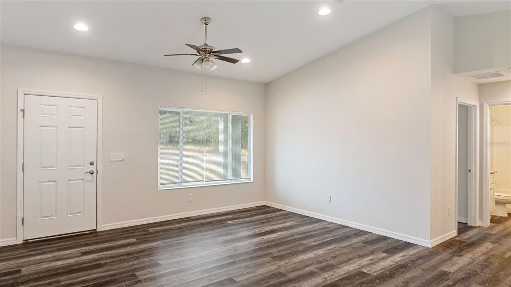 An empty room with wood-look flooring, a ceiling fan, and a white front door — 296 OAK LANE TRACK, OCALA, FL