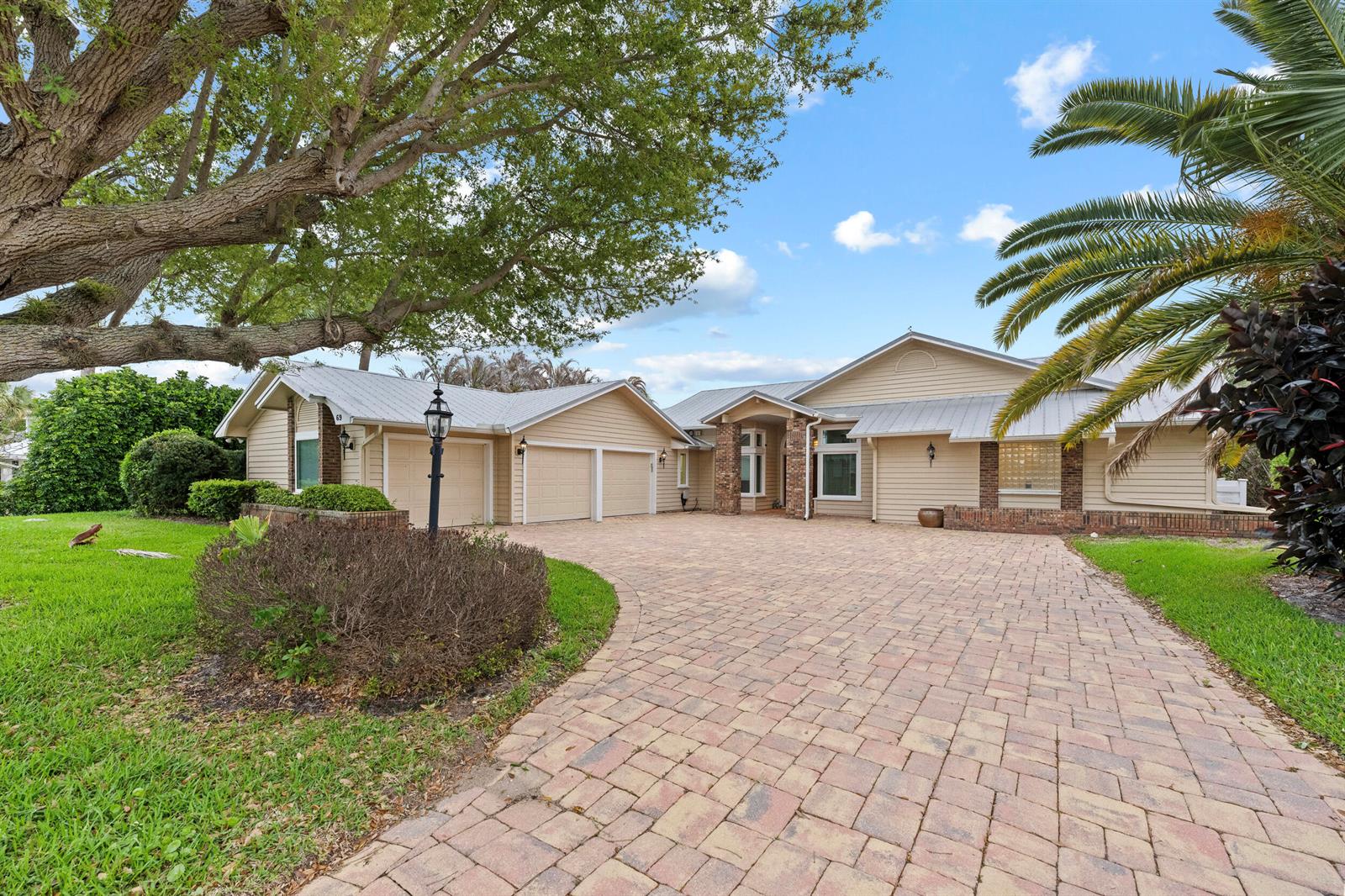 A single-story house with a paved driveway, three-car garage, and a large oak tree — 69 Cache Cay Drive, Vero Beach FL 32963, VERO BEACH, FL