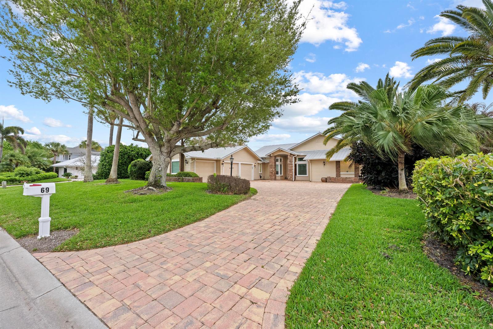 A single-story house with a brick paver driveway, large tree, and palm trees — 69 Cache Cay Drive, Vero Beach FL 32963, VERO BEACH, FL