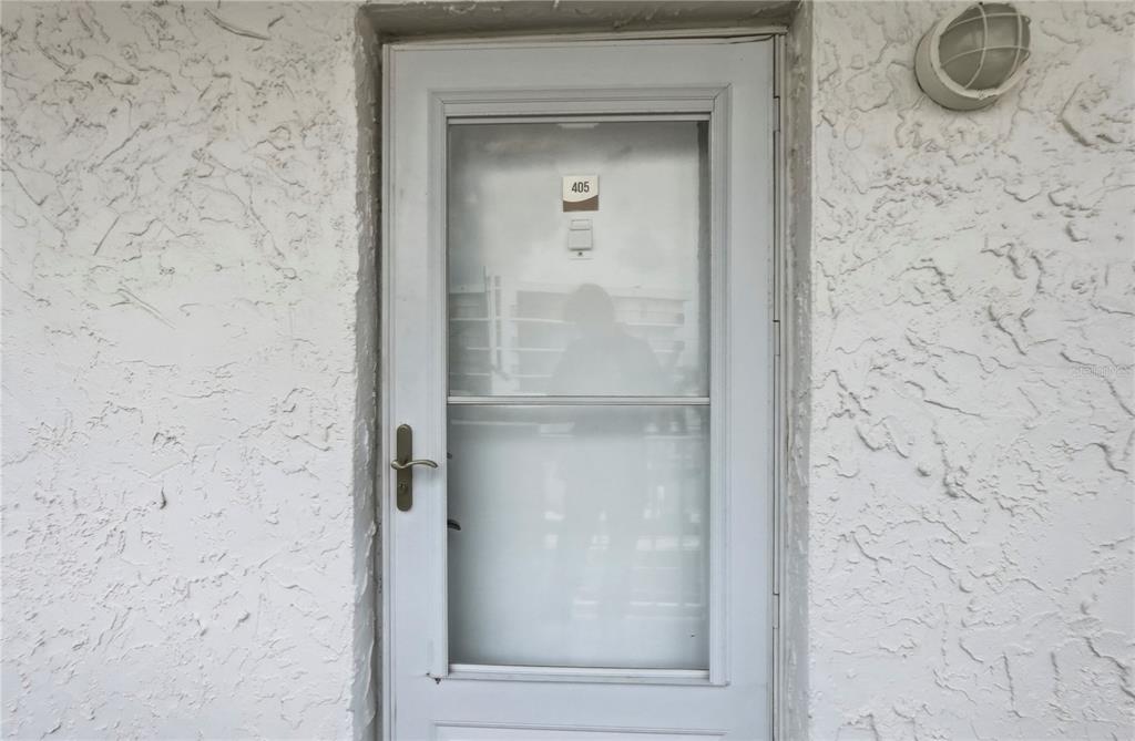 A white storm door with the number 405 is set into a textured white exterior wall — 285 107TH AVENUE UNIT 405, ST PETERSBURG, FL