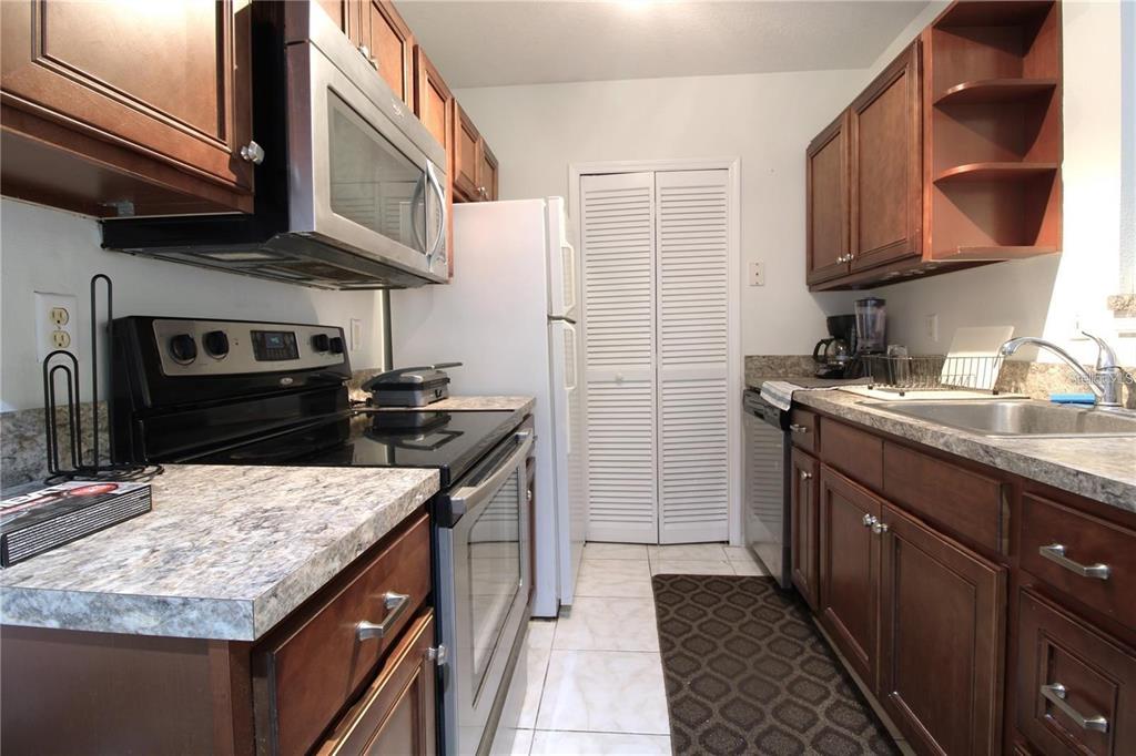 A galley kitchen features dark wood cabinets, stainless steel appliances, and light-colored laminate countertops — 4320 S KIRKMAN ROAD UNIT 1501, ORLANDO, FL