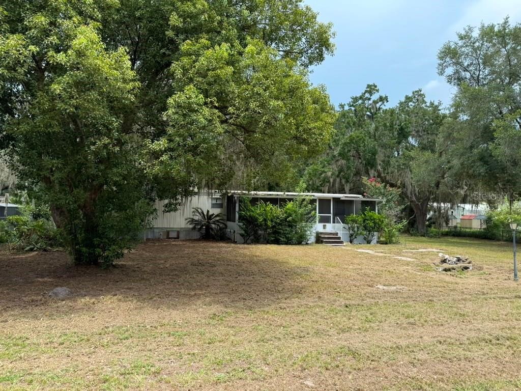 A single-story mobile home with a screened-in porch sits on a grassy, tree-filled lot — 27416 WALNUT AVENUE, OKAHUMPKA, FL