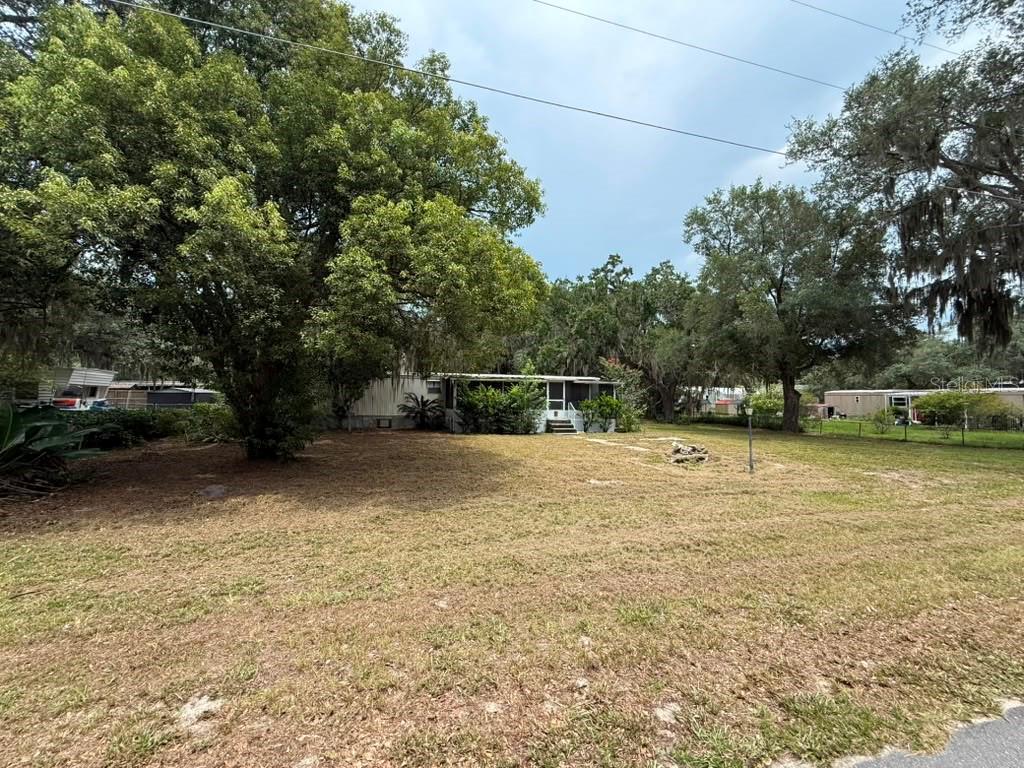 A single-story mobile home sits on a large, grassy lot shaded by mature trees — 27416 WALNUT AVENUE, OKAHUMPKA, FL