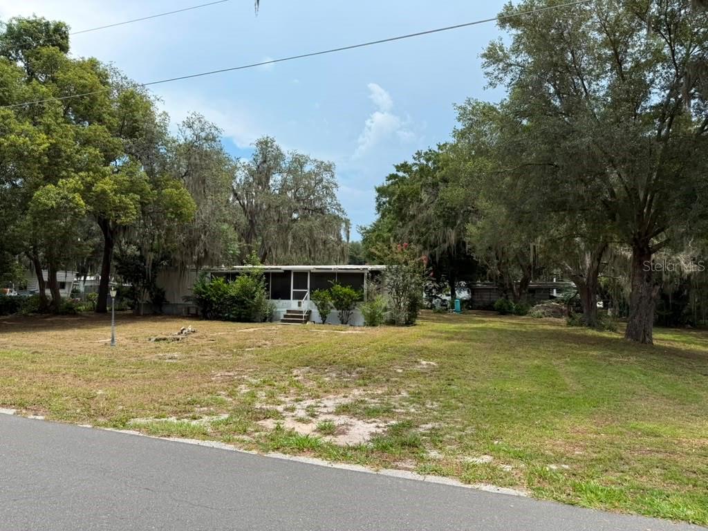 A single-story mobile home sits on a grassy lot surrounded by large, moss-covered trees — 27416 WALNUT AVENUE, OKAHUMPKA, FL