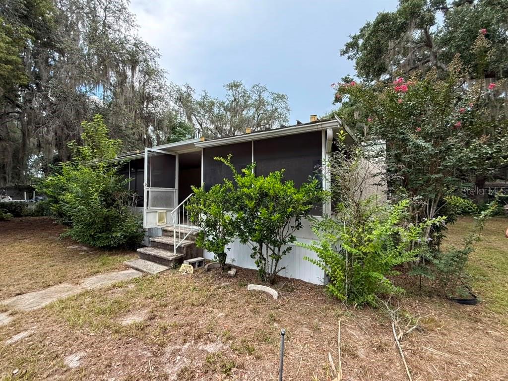 A single-story house with a screened-in porch and concrete steps surrounded by trees — 27416 WALNUT AVENUE, OKAHUMPKA, FL