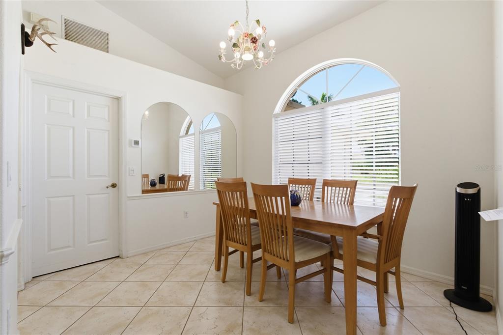 A dining room with tile floors, a wooden table, six chairs, and a large arched window — 257 BROADMOOR LANE, ROTONDA WEST, FL