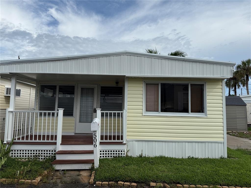 A yellow mobile home features a front porch with white railings and wooden steps — 2601 GULF DRIVE N UNIT 506, BRADENTON BEACH, FL