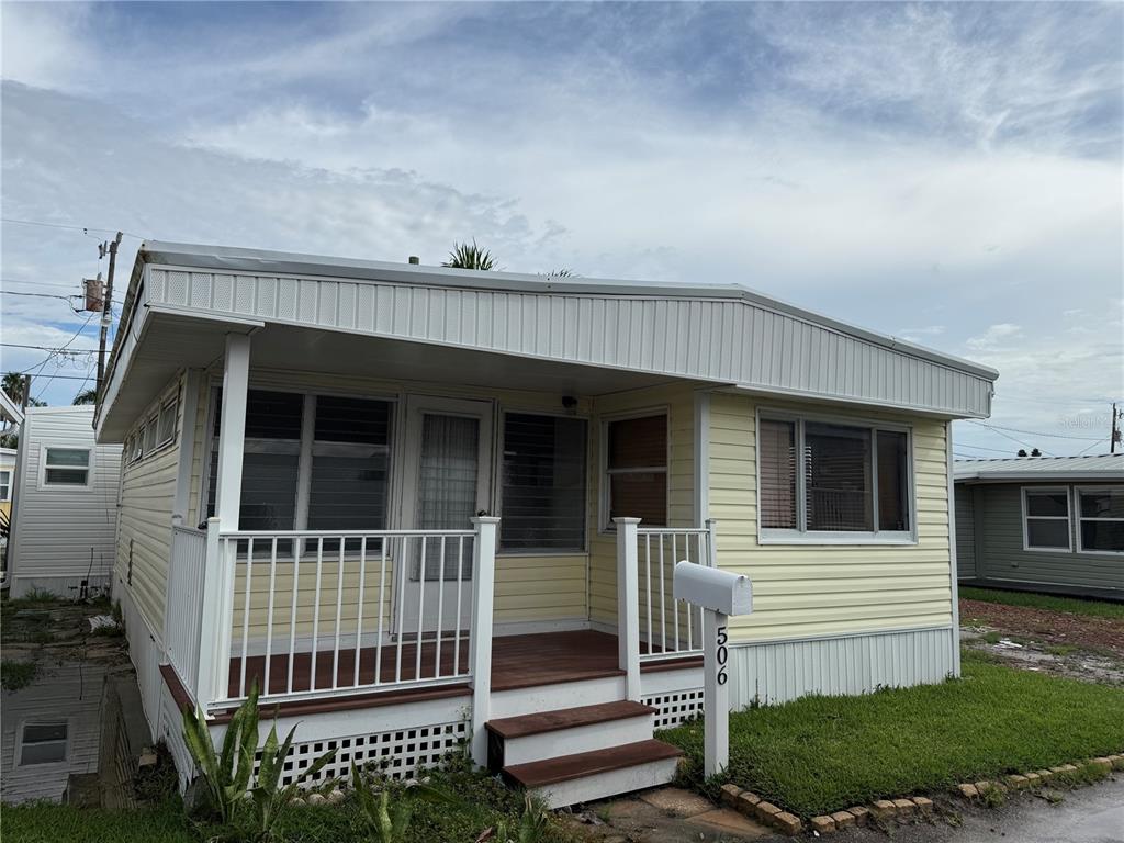 A light yellow mobile home features a front porch with white railings and wooden steps — 2601 GULF DRIVE N UNIT 506, BRADENTON BEACH, FL