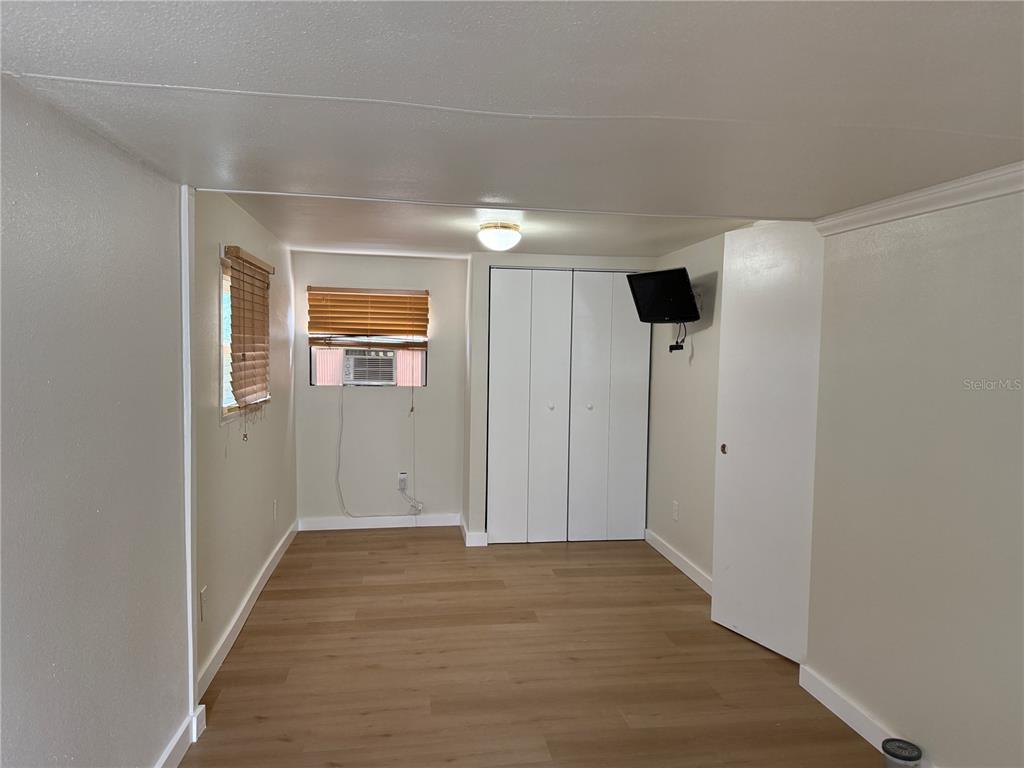 A bedroom features light wood-look flooring, white walls, a closet, and a window air conditioner — 2601 GULF DRIVE N UNIT 506, BRADENTON BEACH, FL