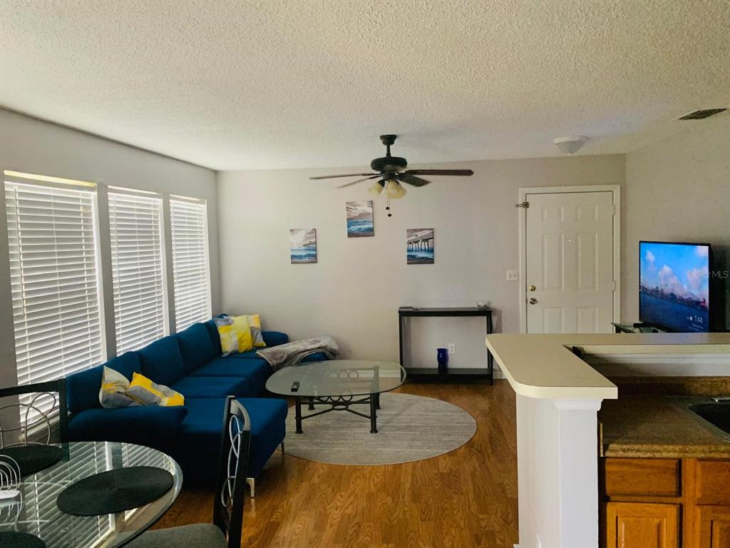 A living room features a blue sectional sofa, a glass coffee table, and wood flooring — 1057 S HIAWASSEE ROAD UNIT 1918, ORLANDO, FL