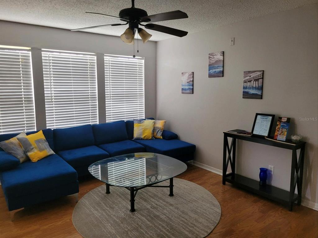 A living room features a blue sectional sofa, a glass coffee table, and wall art — 1057 S HIAWASSEE ROAD UNIT 1918, ORLANDO, FL