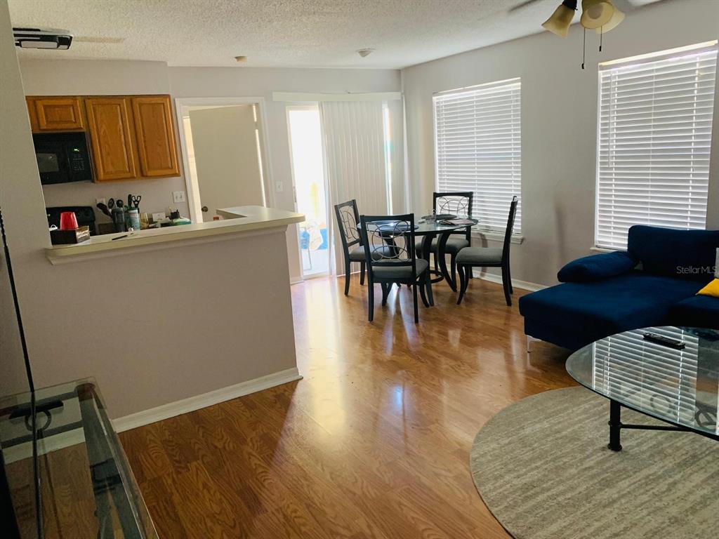 An open-concept living and dining area features hardwood floors, a blue sectional, and kitchen access — 1057 S HIAWASSEE ROAD UNIT 1918, ORLANDO, FL