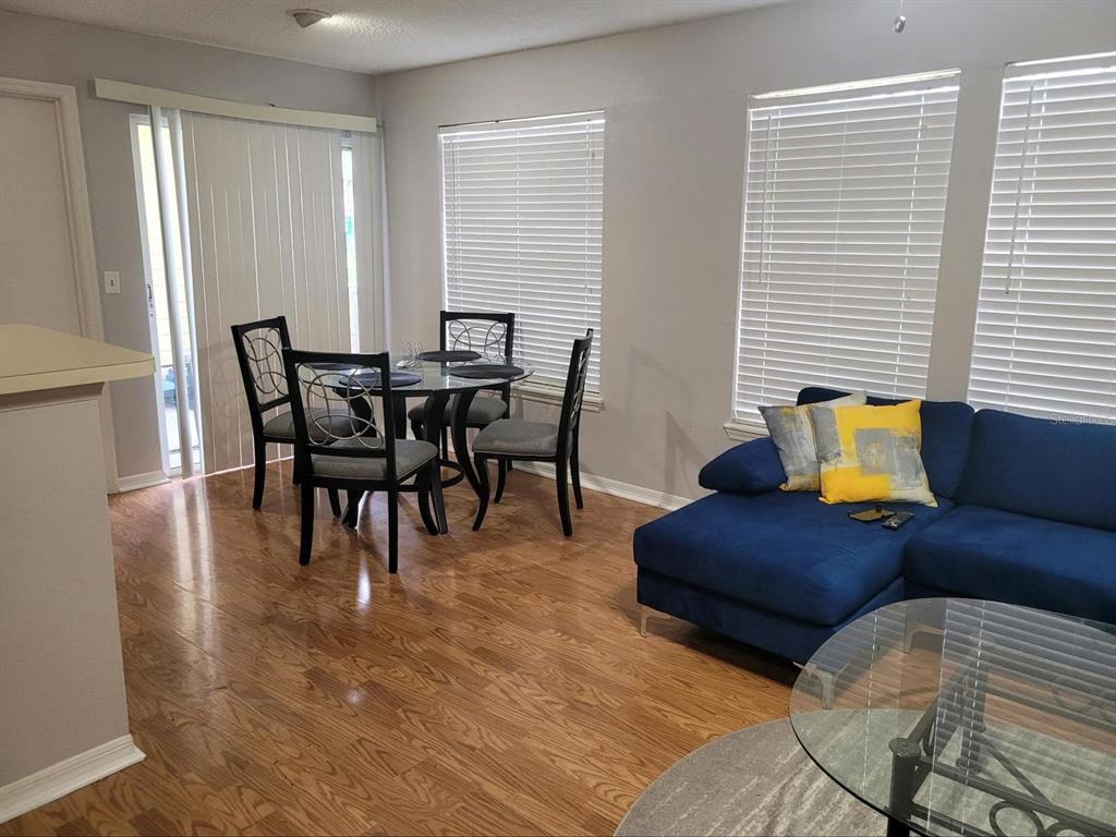 A dining area with a glass table and a blue sectional sofa on hardwood floors — 1057 S HIAWASSEE ROAD UNIT 1918, ORLANDO, FL