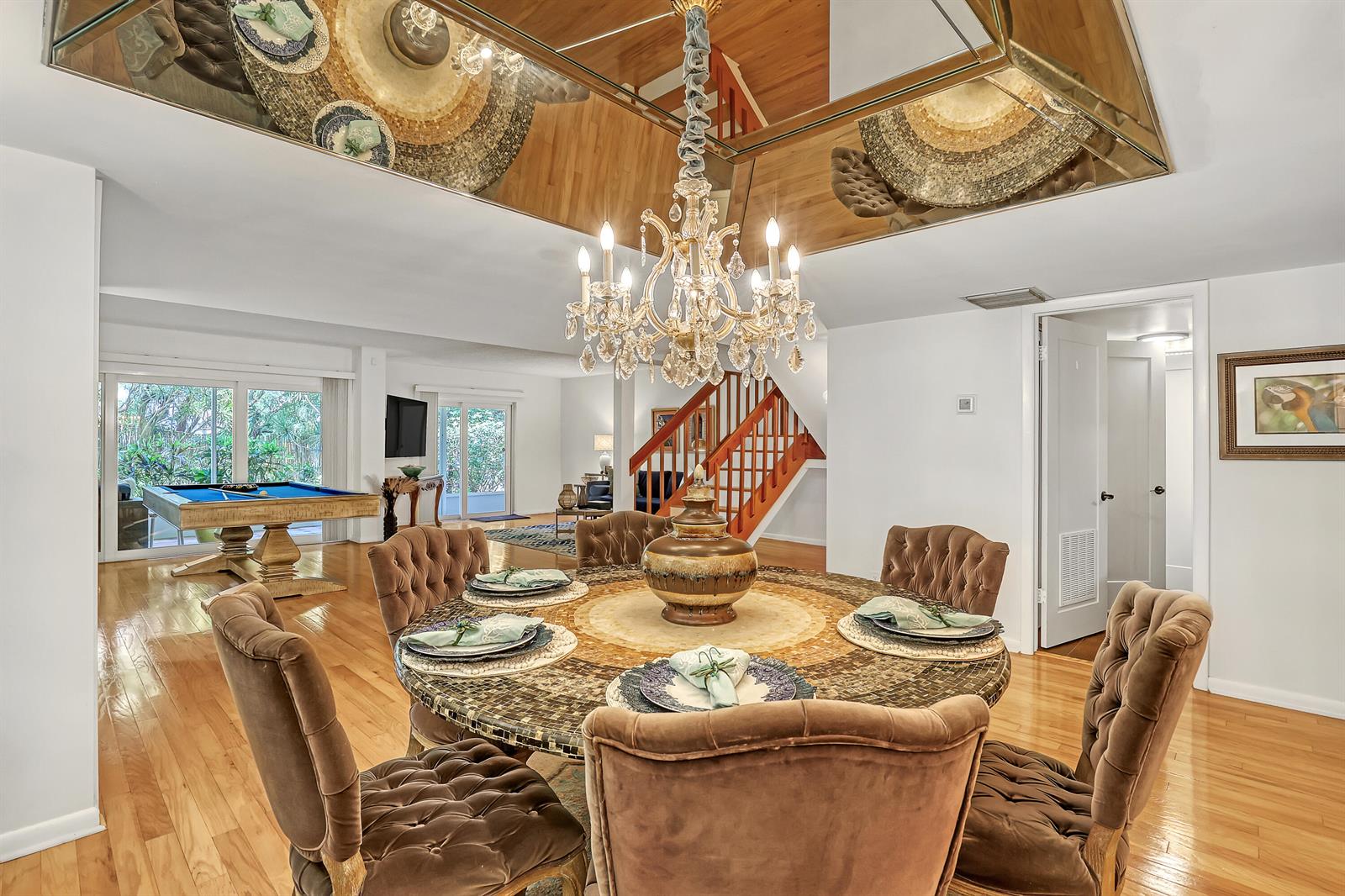 A dining room features a round mosaic table, tufted chairs, a crystal chandelier, and mirrored ceiling — 1100 Surf Road # 104, Singer Island FL 33404, SINGER ISLAND, FL