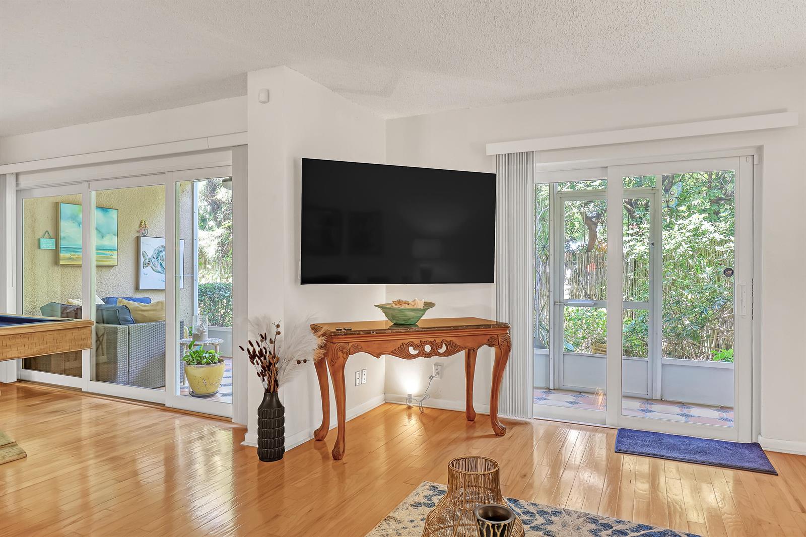 A living room features a wall-mounted television above a wooden console table and sliding doors — 1100 Surf Road # 104, Singer Island FL 33404, SINGER ISLAND, FL