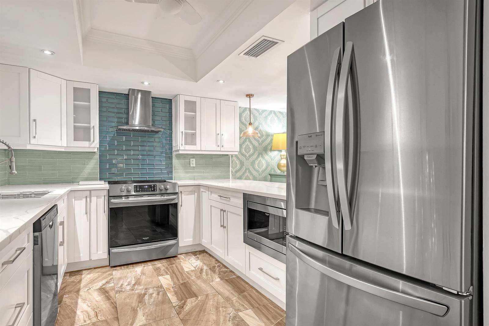 A kitchen with white cabinets, stainless steel appliances, blue subway tile backsplash, and marble floors — 1100 Surf Road # 104, Singer Island FL 33404, SINGER ISLAND, FL