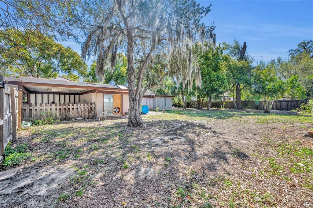 A backyard with a large tree, a covered patio, and a wooden privacy fence — 1560 LAKEHURST AVENUE, WINTER PARK, FL