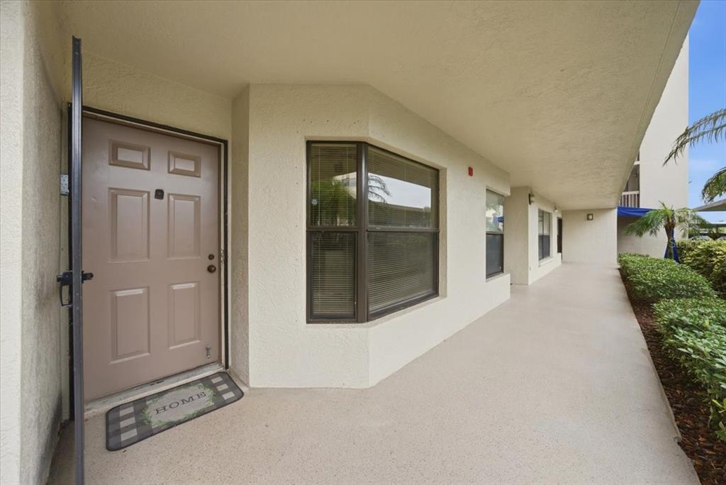 A tan front door with a welcome mat sits on a covered concrete walkway — 1332 PASADENA UNIT 102, SOUTH PASADENA, FL